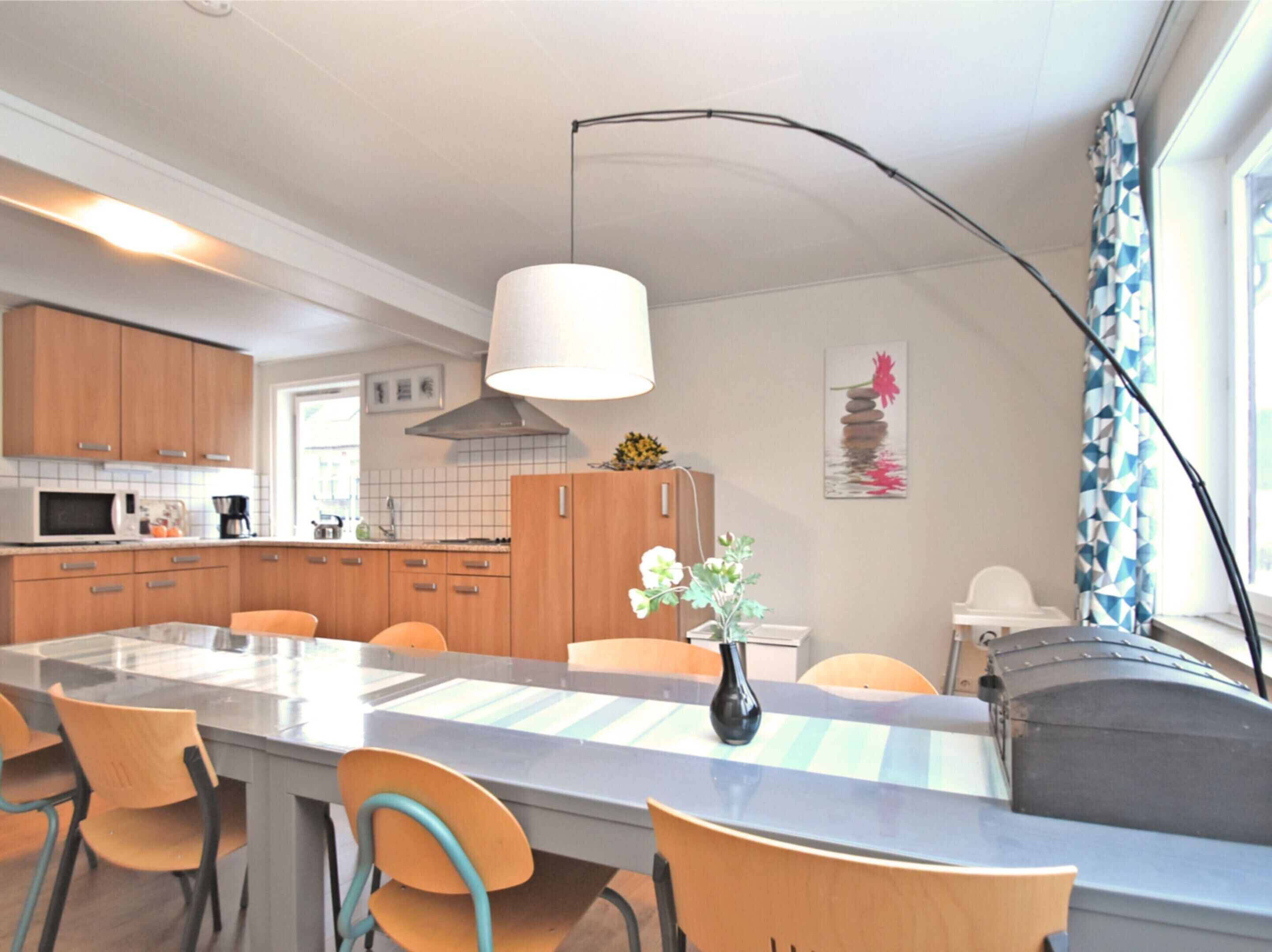 Una cocina moderna con armarios de madera, una isla central con sillas, una lámpara colgante y un jarrón decorativo.