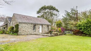 A stone cottage with a sloped roof, a small porch, and a well-maintained lawn. - Secluded Holiday Home in Ceredigion With Garden (Llanon)