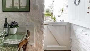 A room with a table set for two, a clock on the wall, and a view of the outside. - Secluded Holiday Home in Ceredigion With Garden (Llanon)