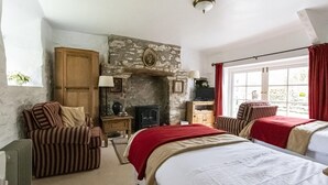 A cozy room with a stone fireplace, two beds, a wooden wardrobe, and a window with curtains. - Secluded Holiday Home in Ceredigion With Garden (Llanon)
