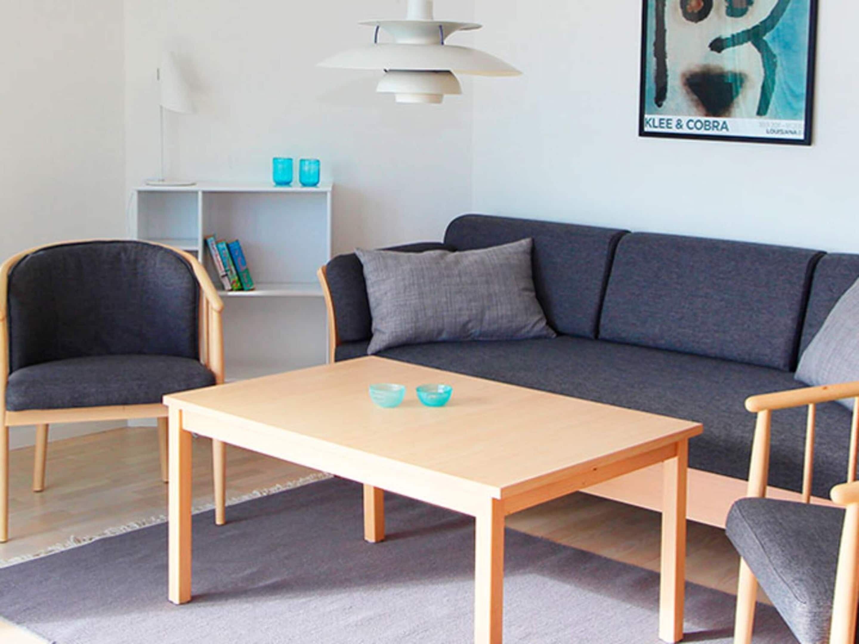 A modern living room with a grey sofa, two matching armchairs, a wooden coffee table, and a white pendant light.