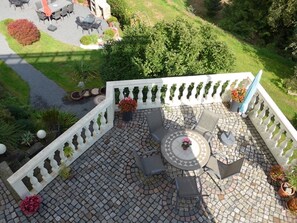 Eine Terrasse mit einem runden Tisch und Stühlen, umgeben von Kübelpflanzen und einem weißen Geländer.