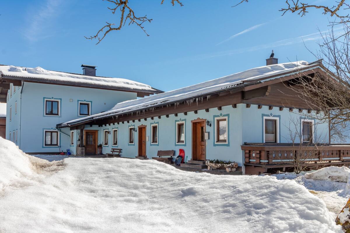 A traditional chalet with a snow-covered roof, wooden exterior, and a small porch area.