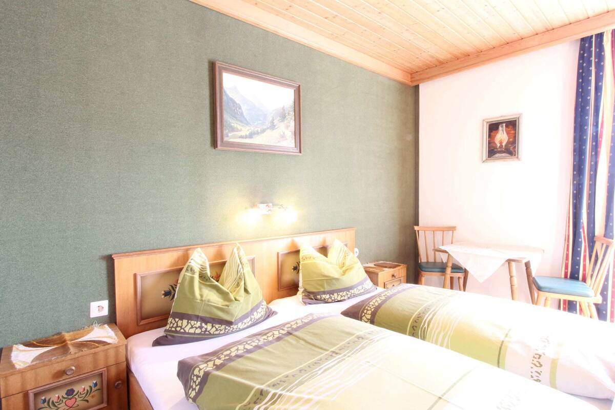 A hotel room with two beds, a wooden headboard, a small table, and a chair.