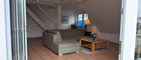En stue med en modulsofa, et træ sofabord og en lampe. Der er en trappe, der fører op til en etage.