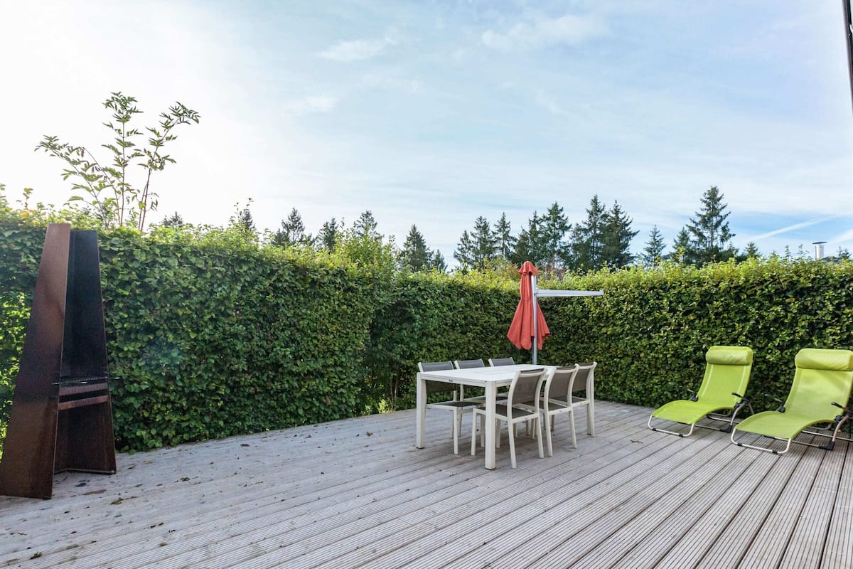 A deck with a table and chairs, a TV, and a hedge in the background.