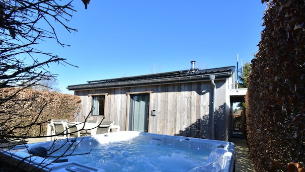 A hot tub in a backyard with a wooden fence and a building in the background. - Boutique Chalet in Bullingen Near Lake (Buellingen)