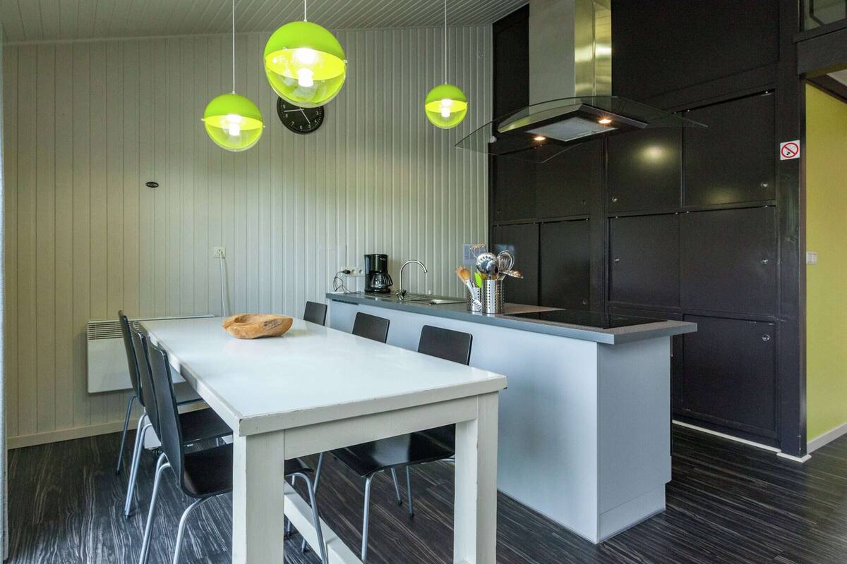 A modern kitchen with a white countertop, black cabinets, and a black stove. There are three hanging green lights above the counter.