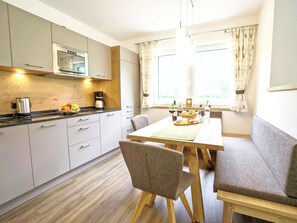 A modern kitchen with a dining area, wooden cabinets, a coffee maker, and a window with curtains.