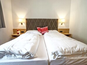 A double bed with white linens, a diamond-patterned headboard, bedside lamps, and a nightstand with a bottle.
