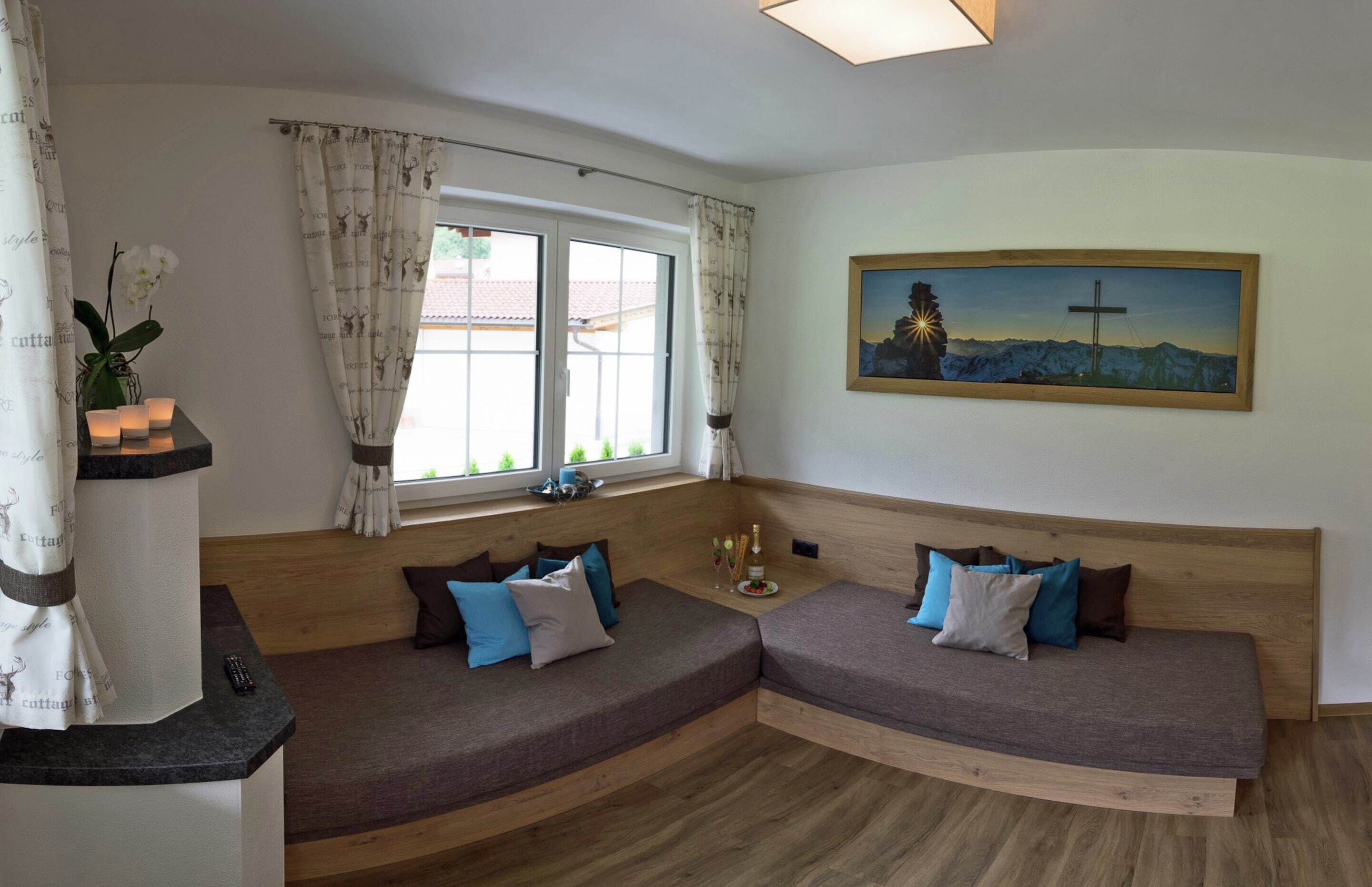A cozy room with a curved wooden bench, a painting of a mountain landscape, and a window with curtains.