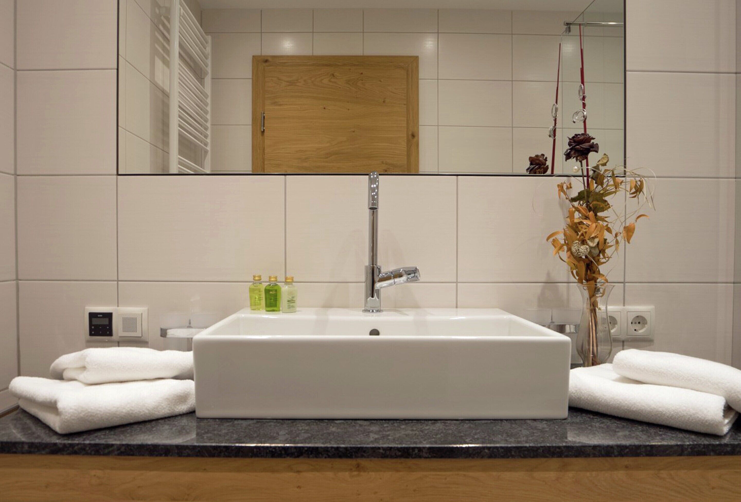A bathroom with a white sink, a wooden cabinet, a mirror, and a vase with dried flowers.