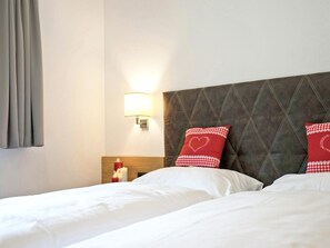 A hotel room with two beds, a nightstand with a candle, a wall-mounted lamp, and a checkered pillow.