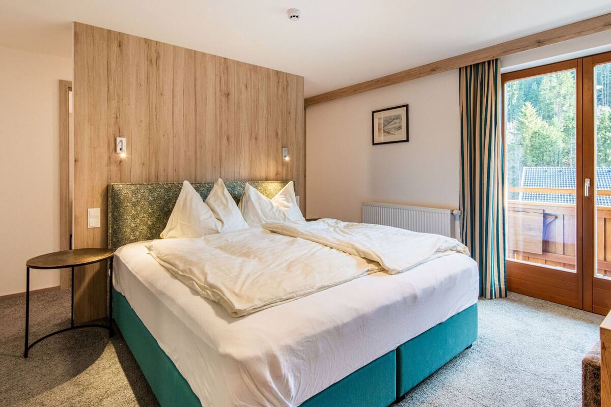 A bedroom with a bed, a nightstand, a window with curtains, and a radiator.