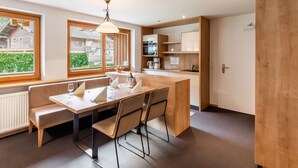 A modern kitchen with wooden cabinets, a dining table with chairs, and a view of the outside through large windows. - Lovely Apartment With Sauna, Ski Storage, Pool, Terrace (Wald im Pinzgau)