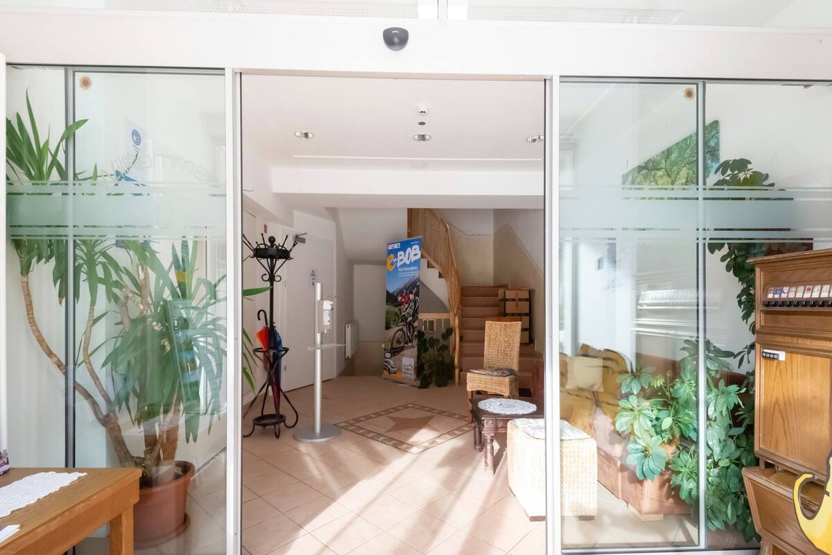 A spacious room with a tiled floor, a wooden bench, a potted plant, a wicker chair, a small round table, and a piano.