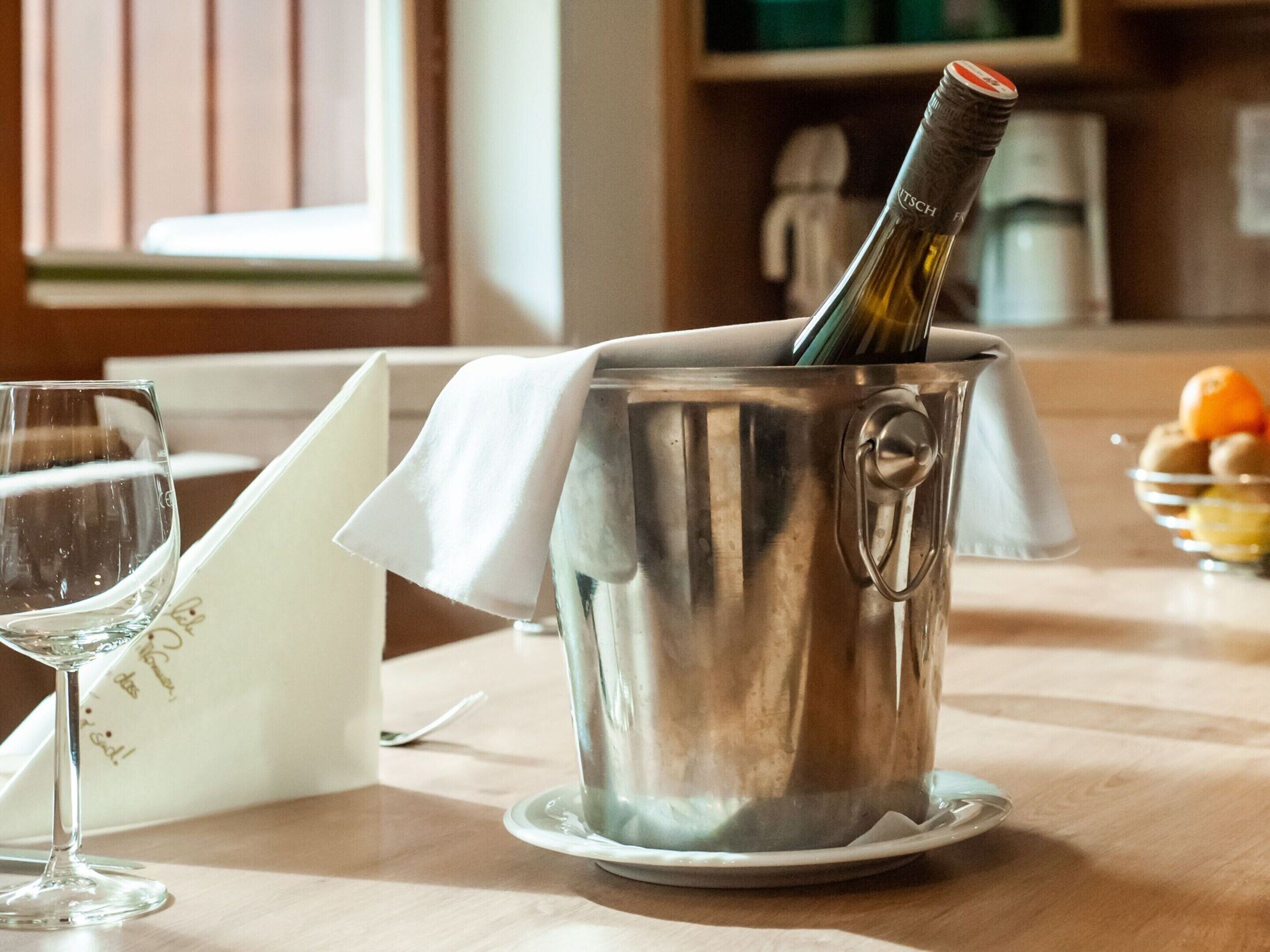 A stainless steel wine cooler with a bottle of wine, a glass, and a napkin on a wooden table.