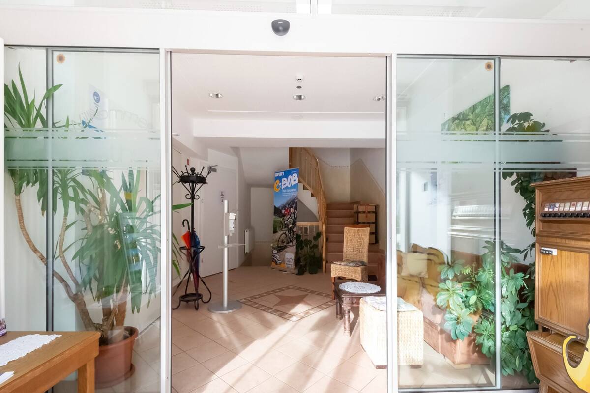 A spacious room with a tiled floor, a wooden bench, a potted plant, a glass door, a coat rack, and a staircase leading to another level.