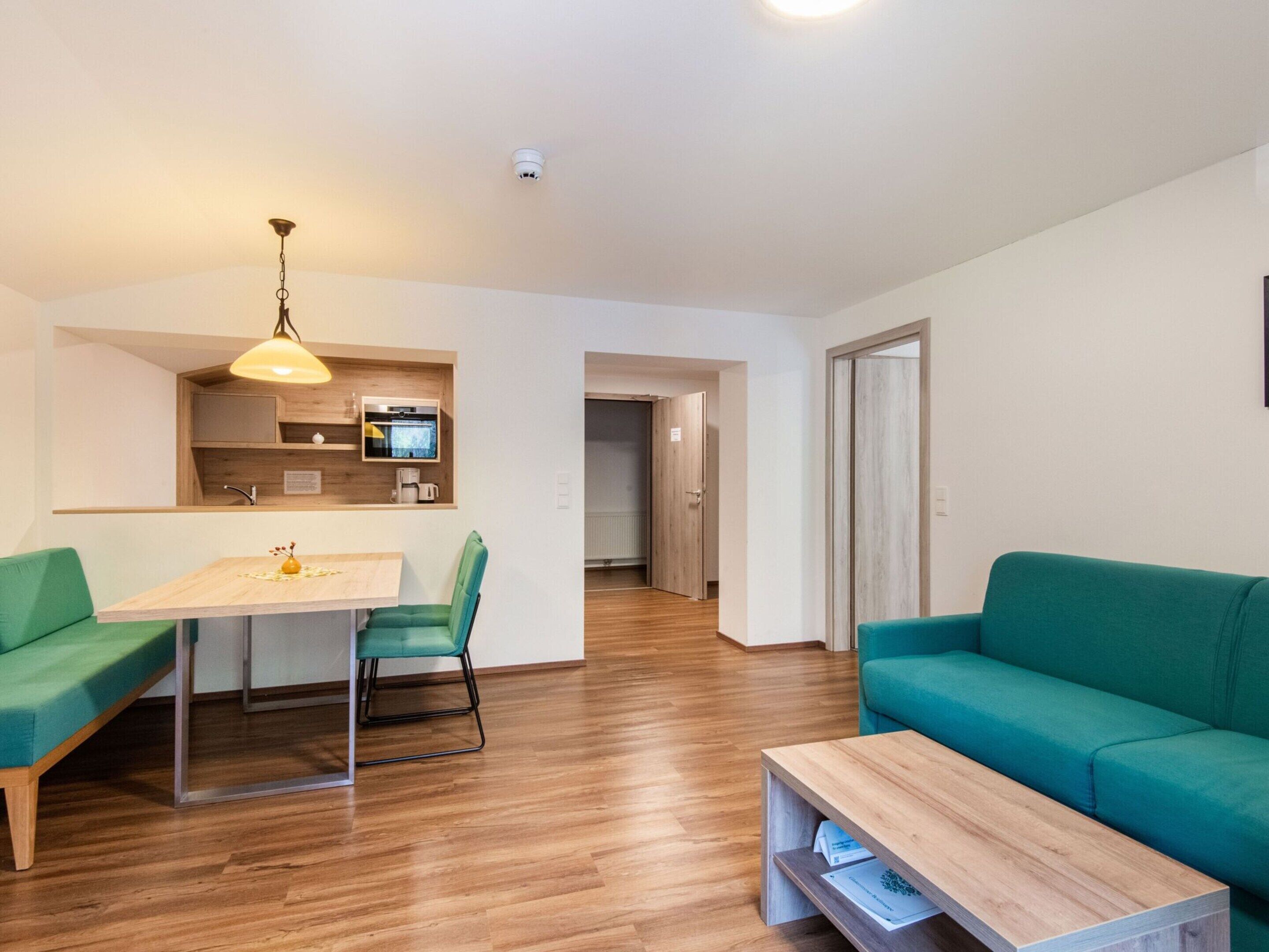 A modern living room with a wooden floor, a green sofa, a wooden coffee table, and a dining area with a table and chairs.
