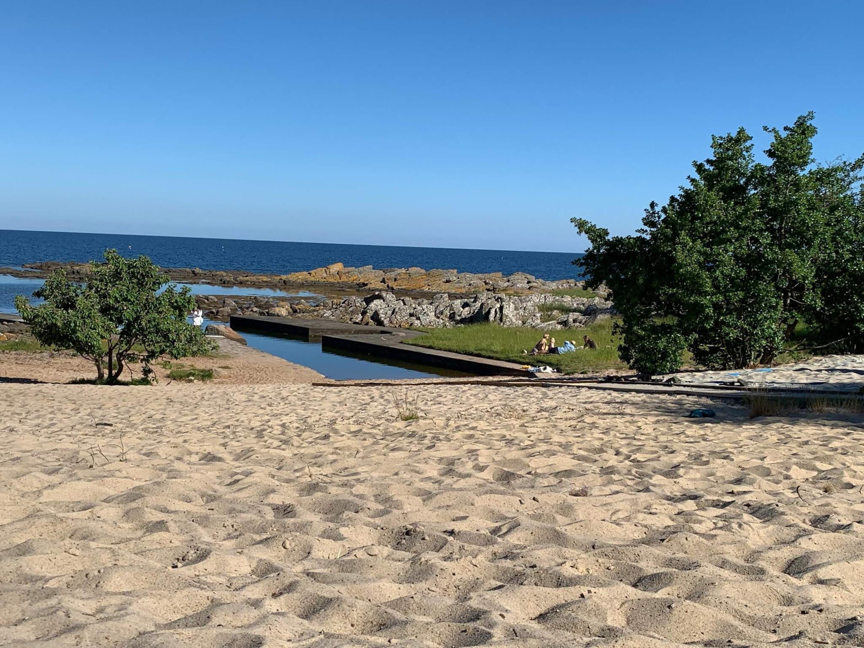A sandy beach with a rocky shoreline, a small water channel, and a few trees.