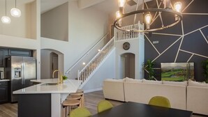 Eine moderne Küche mit einer zentralen Kochinsel, ein Essbereich mit einem schwarzen Tisch und eine Treppe, die in eine obere Ebene führt.