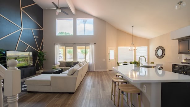 Ein modernes Wohnzimmer mit einer großen Couch, einer Essecke mit Hockern und einer Küche mit Kochinsel.