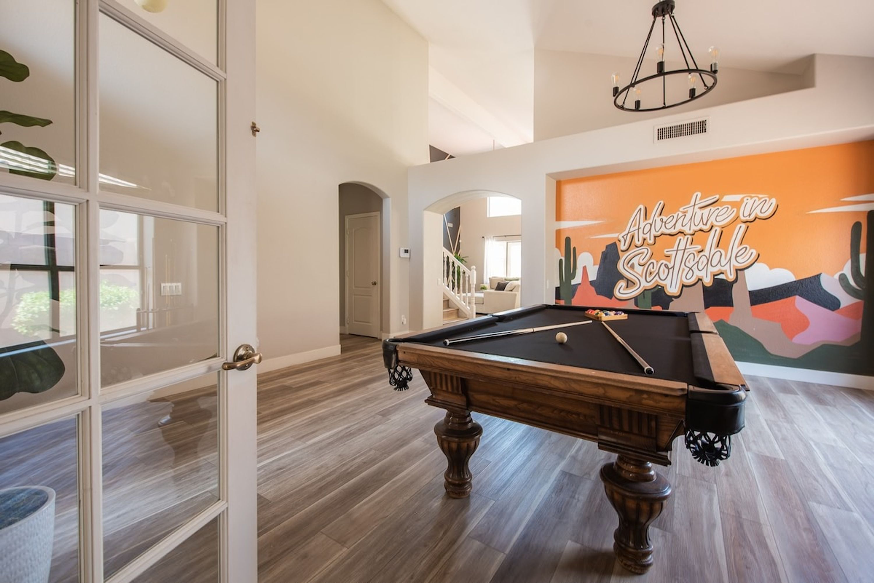 A pool table in a room with a modern design, a staircase, and a mural with the text "Adventive in Scottsdale".