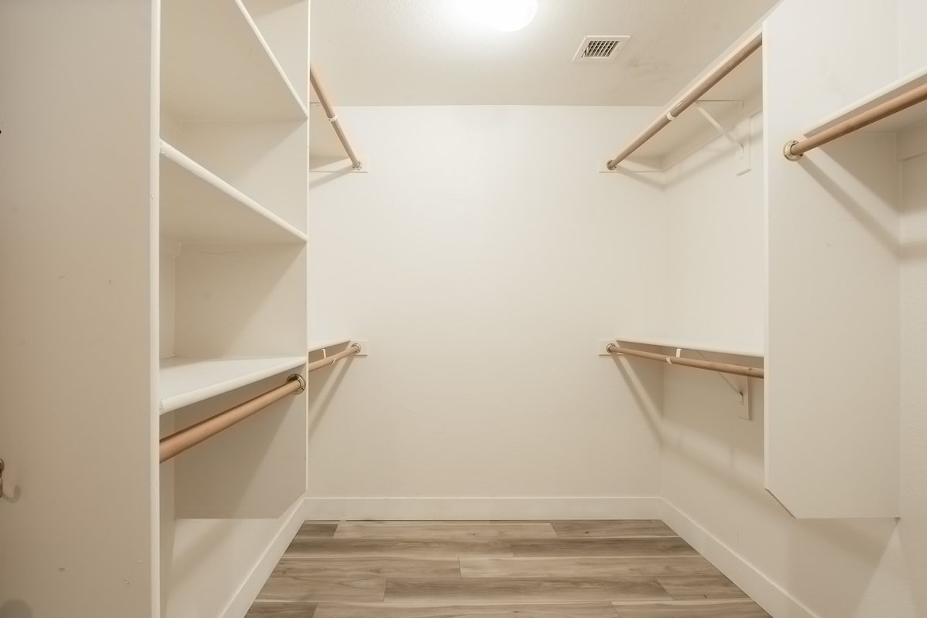 A walk-in closet with white walls and wooden flooring.