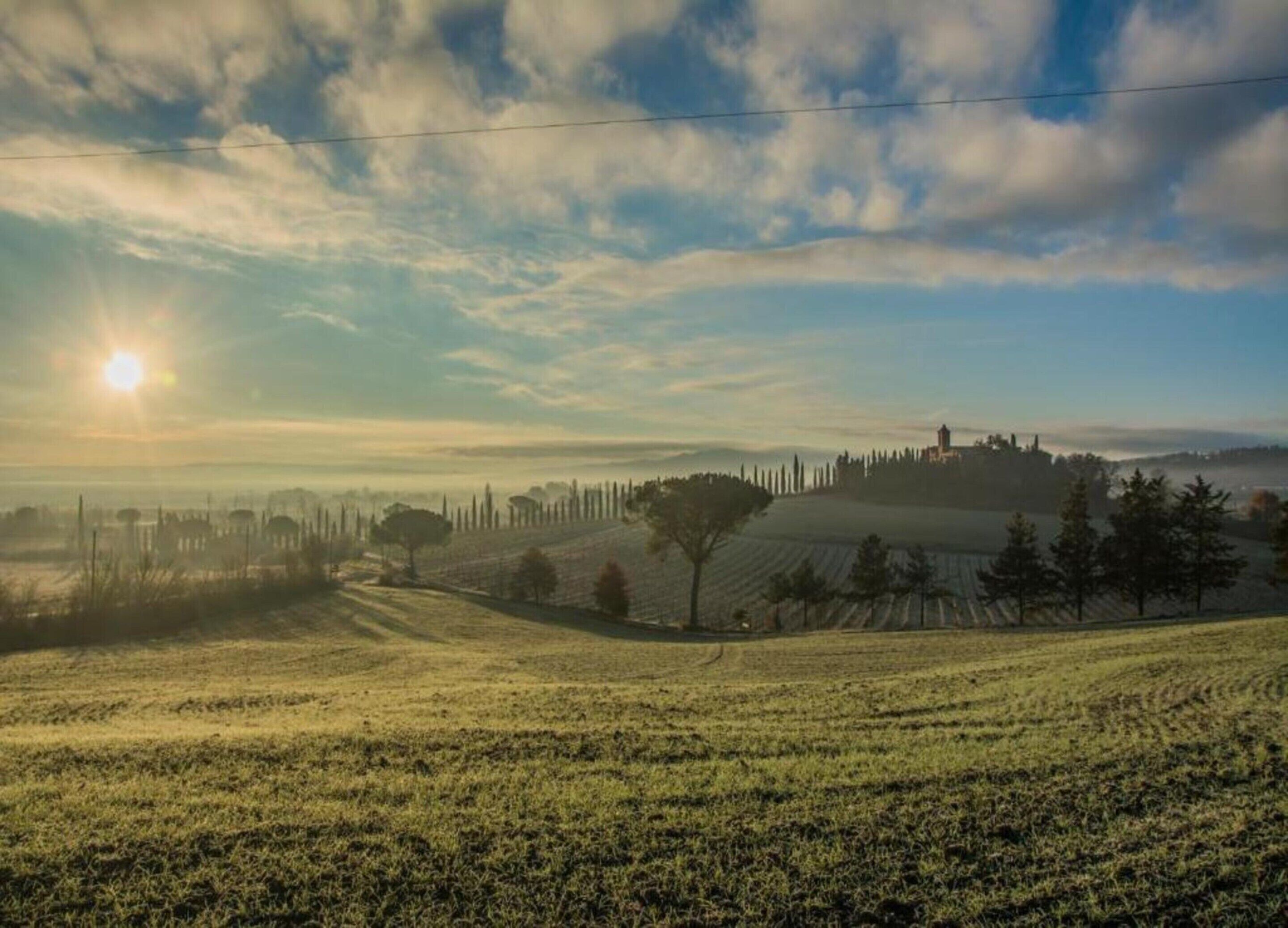 A rural landscape with rolling hills, a clear sky, and a distant building.