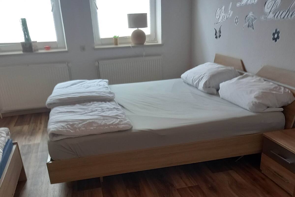 A neatly made bed in a room with wooden flooring, a window with blinds, and a wall with decorative butterfly decals.