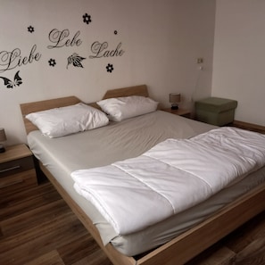 A single bed with a wooden frame and white bedding, a bedside table with a lamp, a green ottoman, and a wall with decorative decals. - Apartment in the Hochsauerland Region in a Quiet Location (Diemelsee)
