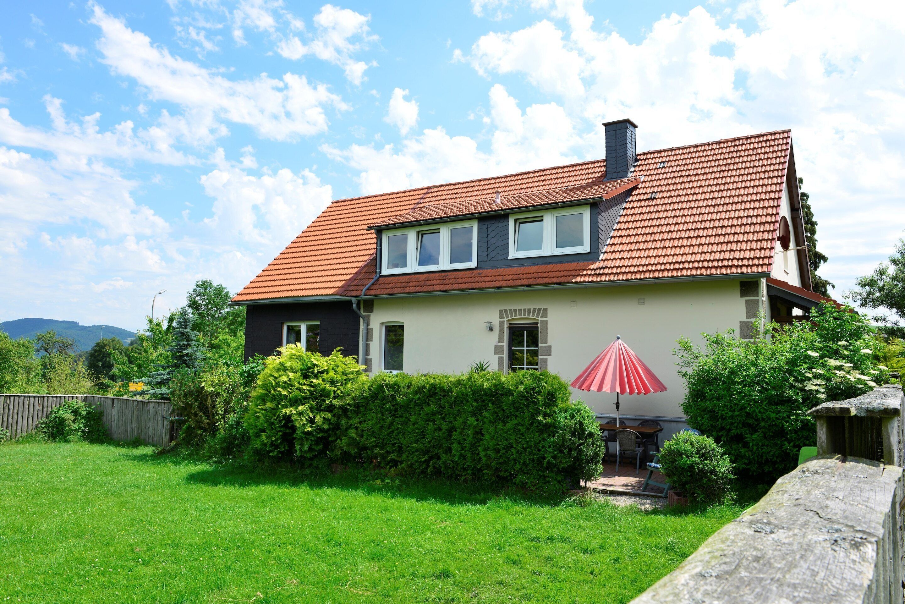Ein zweistöckiges Haus mit rotem Ziegeldach, einer kleinen angebauten Garage und einem gepflegten Rasen.