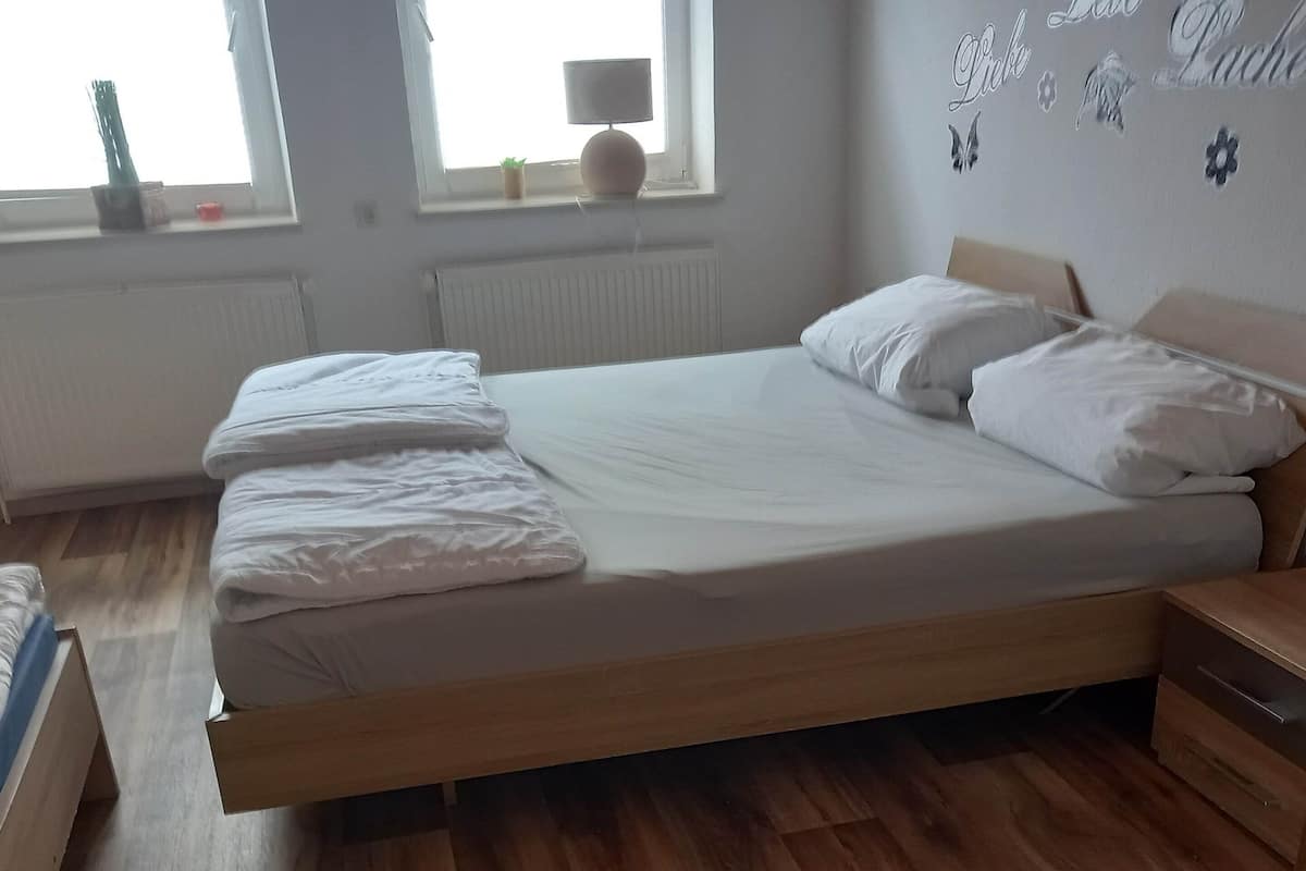 Ein ordentlich bezogenes Bett in einem Zimmer mit Holzboden, einem Fenster mit Jalousien und einer Wand mit dekorativen Schmetterlingsstickern.