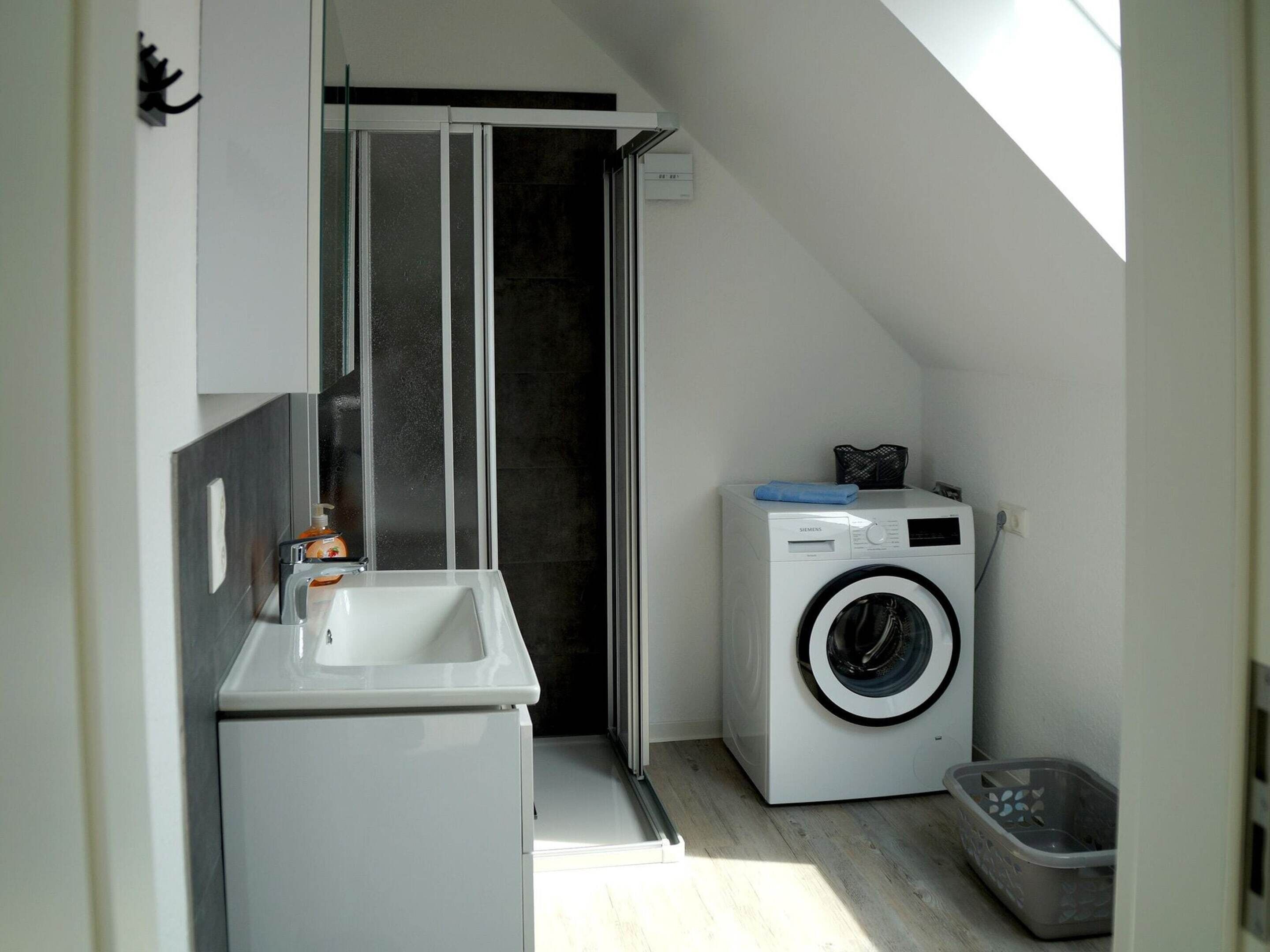 A compact, modern bathroom with a built-in shower, a washing machine, and a sink.
