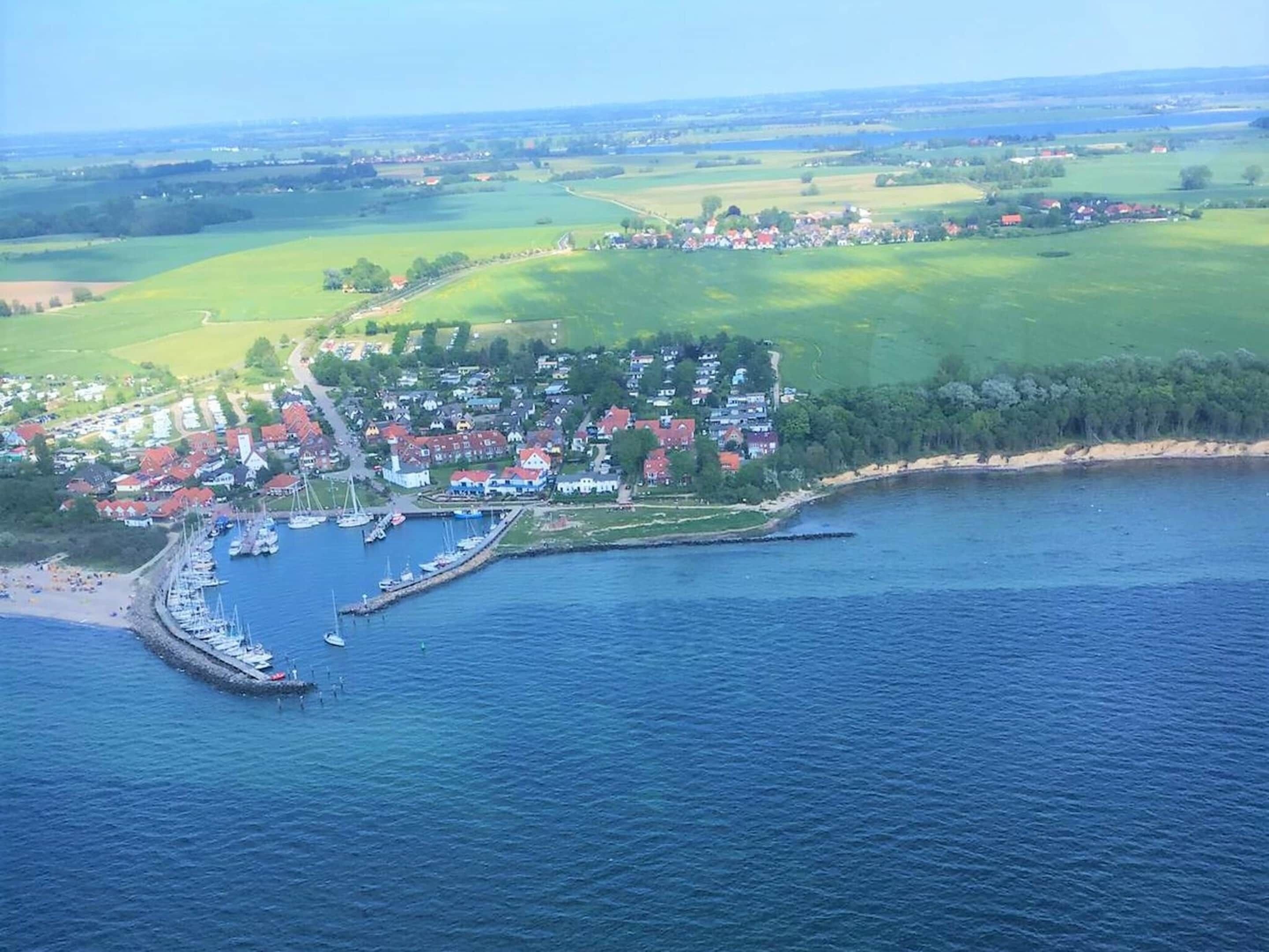 An aerial view of a coastal town with a marina, houses, and surrounding green fields.