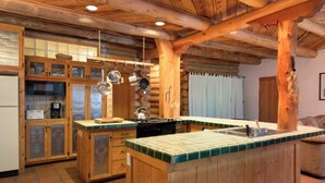 A rustic kitchen with wooden cabinets, a central island, and hanging pots. - Denton Cabin - Warm Log Cabin, close to Mountain Stream and Ski Return Trail (Taos Ski Valley)