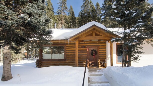 A wooden cabin with a porch, surrounded by snow-covered ground and trees. - Denton Cabin - Warm Log Cabin, close to Mountain Stream and Ski Return Trail (Taos Ski Valley)