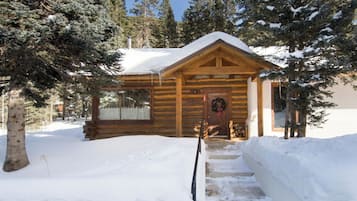 Una cabaña de madera con un porche, rodeada de nieve y árboles.