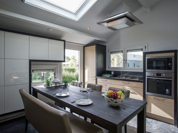 A modern kitchen with a dining area, featuring a skylight, built-in appliances, and a fruit bowl on the table. - Lovely Holiday Home in Kattendijke Near Centre (Kattendijke)