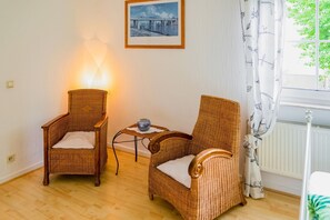 A room with two wicker chairs, a small table with a vase, a framed picture on the wall, and a window with curtains. - Luxurious Apartment in Medebach Near Public Pool (Medebach)