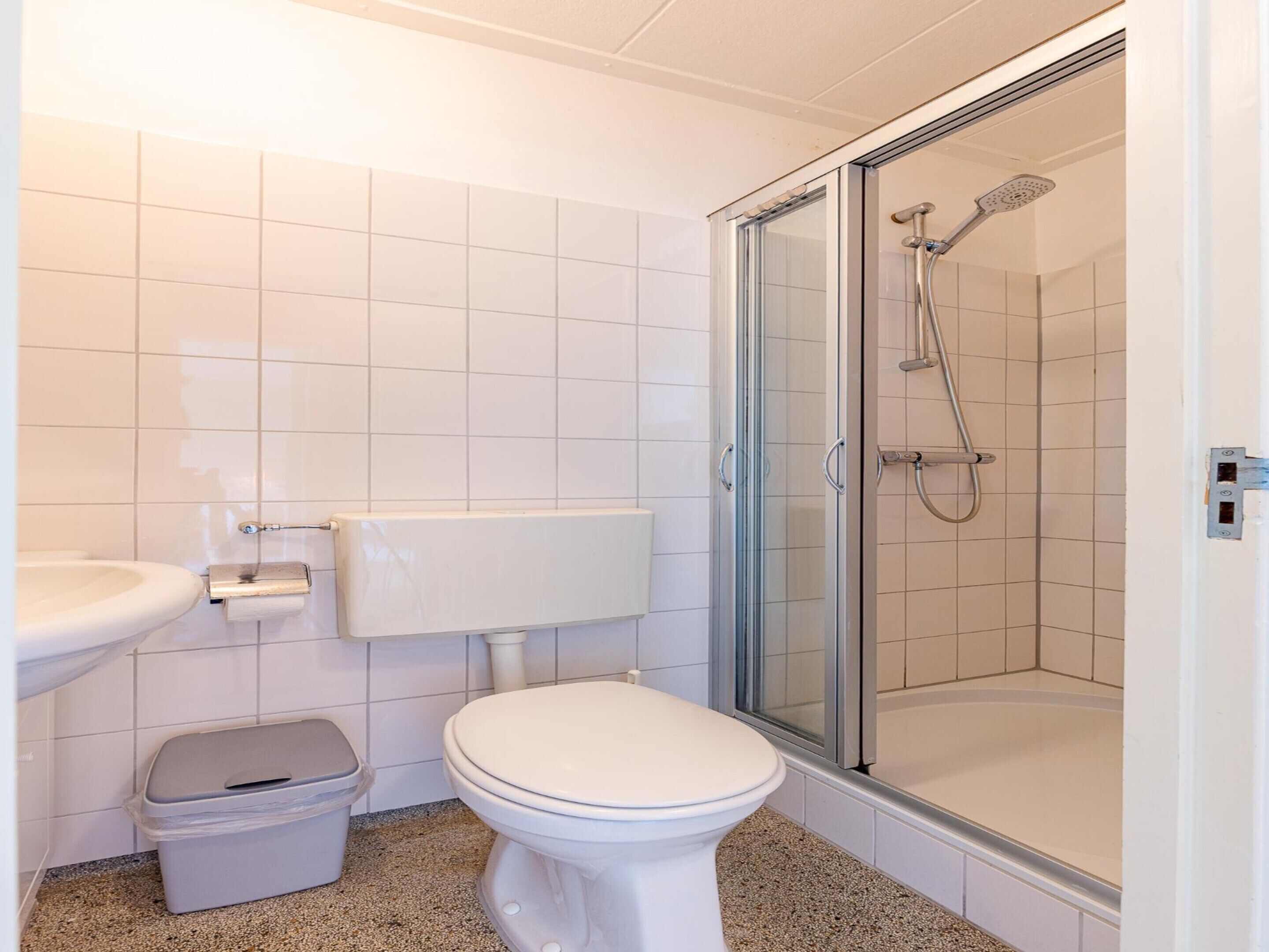 Une salle de bain comprenant des toilettes, un lavabo et une douche fermée par des parois en verre.