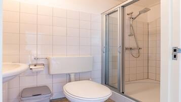 Une salle de bain comprenant des toilettes, un lavabo et une douche fermée par des parois en verre.