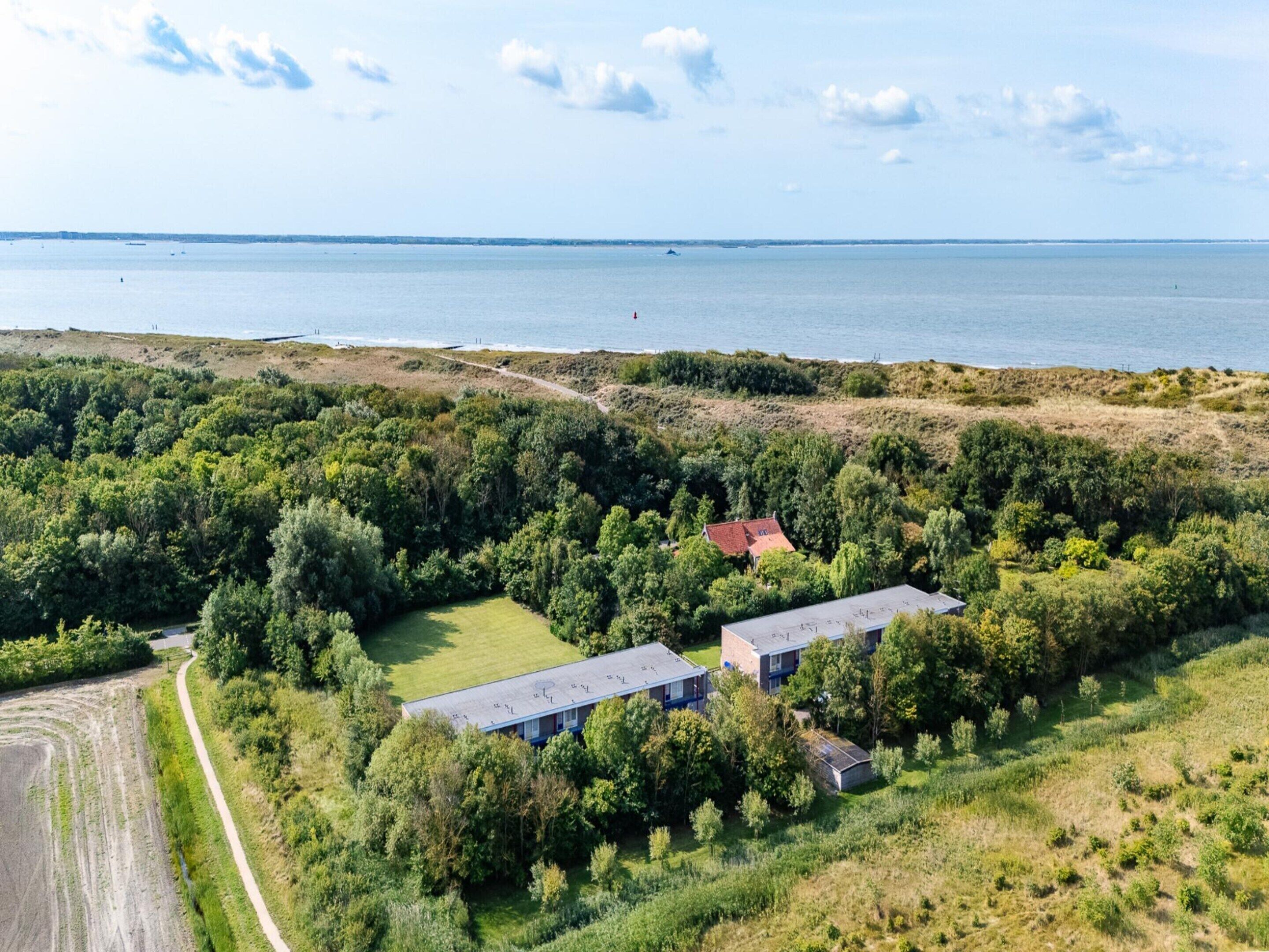 Luftaufnahme einer Anlage mit zwei Gebäuden, umgeben von dichtem Grün und Blick auf die Küste.