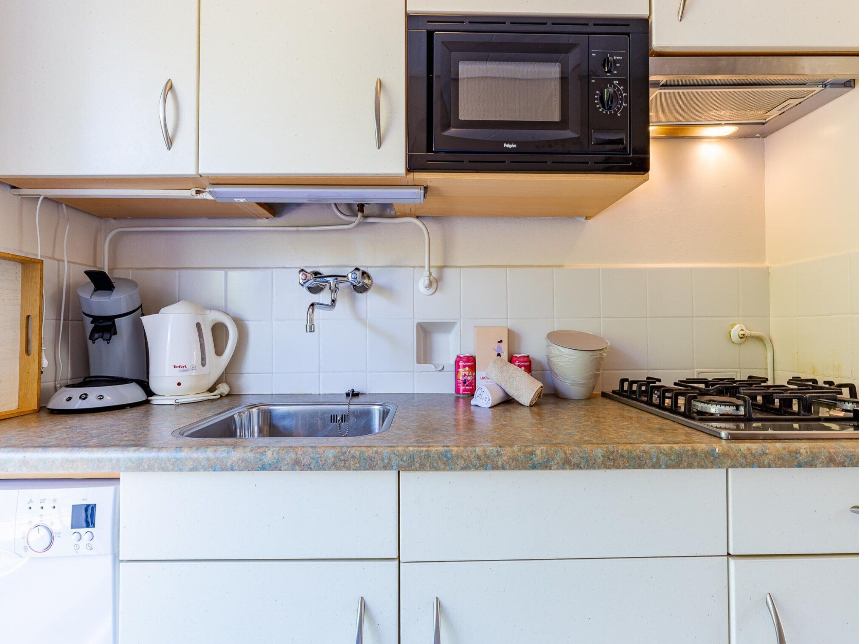 A kitchen with a microwave, coffee maker, kettle, sink, and gas stove.