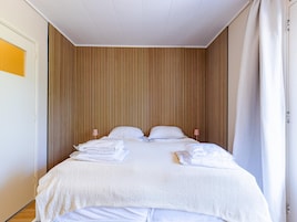 A neatly made bed with white linens and towels, a wooden slat wall, and a white ceiling.