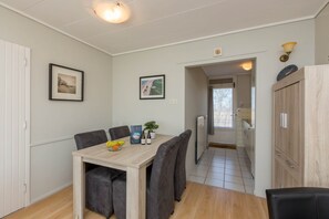 A dining area with a wooden table, grey upholstered chairs, and framed pictures on the wall. - Attractive Apartment Near Vlissingen Beach (Vlissingen)