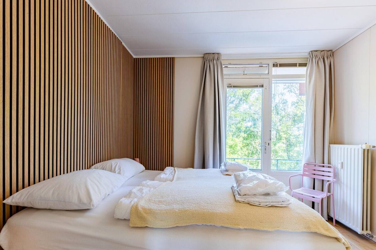 Ein Hotelzimmer mit einem Bett, einem Fenster mit Vorhängen, einem Heizkörper und einem rosa Stuhl.