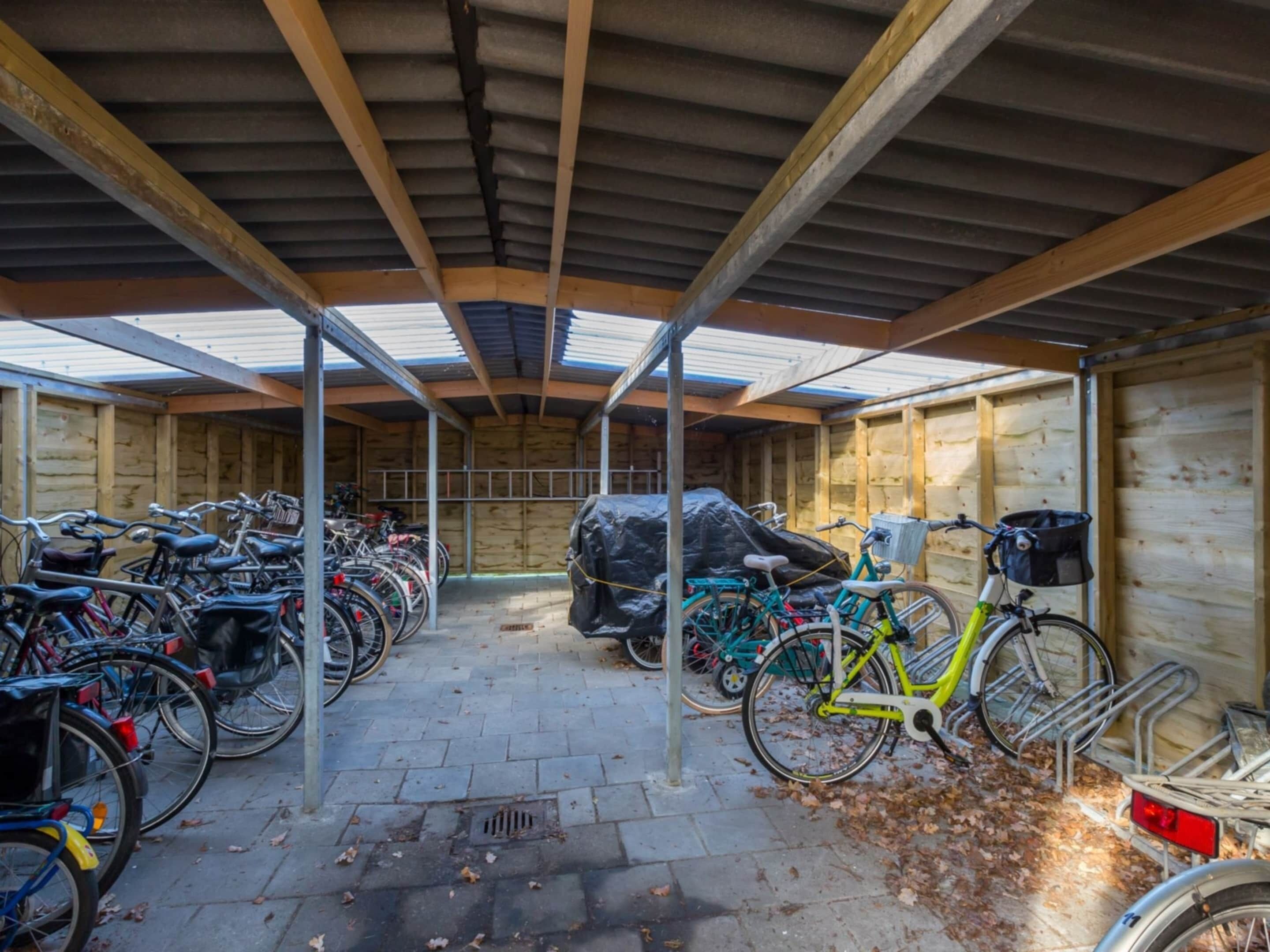 Ein überdachter Fahrradstellplatz mit mehreren Fahrrädern und ein überdachter Stellplatz für Autos.