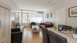 Een moderne woonkamer met een bank, salontafel en een eettafel met wijnflessen en een plant.