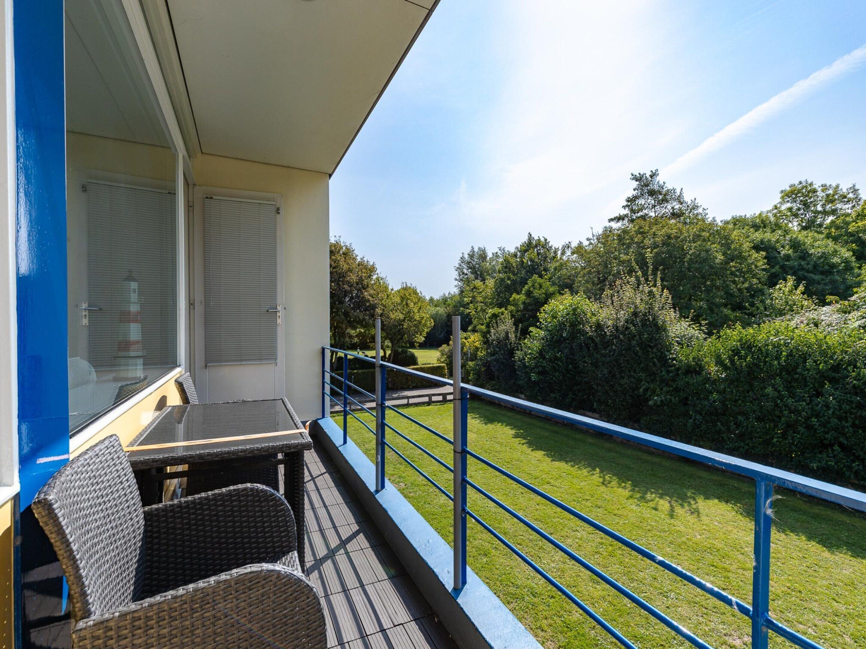 A balcony with wicker furniture, a view of a green landscape, and a clear sky.